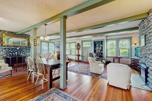 A spacious living room with a stone fireplace, wooden flooring, and a large window.