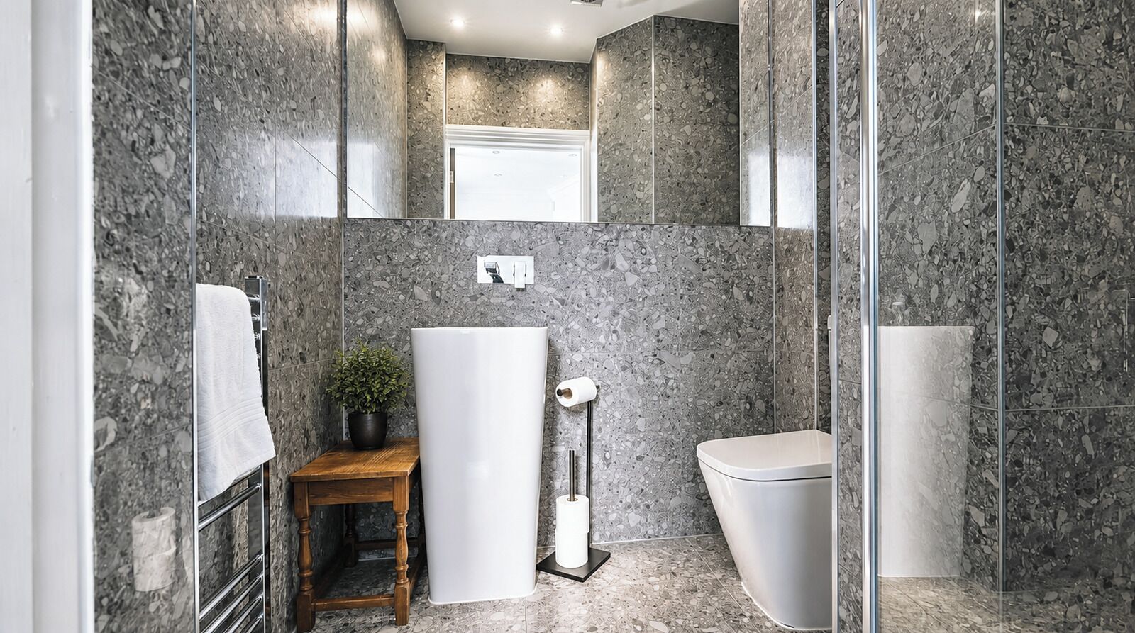 Een badkamer met een marmeren wand, een toilet, een wastafel, een handdoekhouder en een klein tafeltje met een plant.