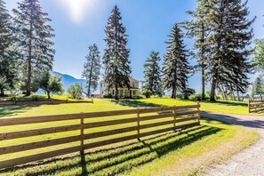 A house surrounded by tall trees and a wooden fence. - Charming Farmhouse on 100 Acres W/ Mountain Views, WiFi, Porch & Livestock (Columbia Falls)