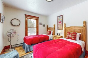 A bedroom with two beds, a standing fan, a window, and a wall-mounted picture. - Charming Farmhouse on 100 Acres W/ Mountain Views, WiFi, Porch & Livestock (Columbia Falls)