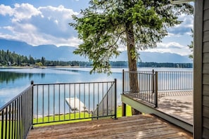 Eine Holzterrasse mit Metallgeländer, die auf einen See mit Bergelände blickt.