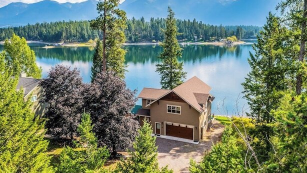 A house with a garage, surrounded by trees and a lake. - Waterfront home on Echo Lake with dock, amazing view, deck & washer/dryer (Bigfork)