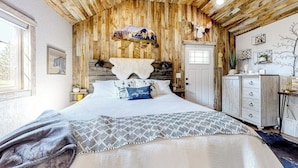 A rustic bedroom with a wooden ceiling, a bed with patterned bedding, a mounted animal head, and a door with a window. - Rustic getaway with fireplace, patio area, board games, full kitchen, & TV (Kalispell)