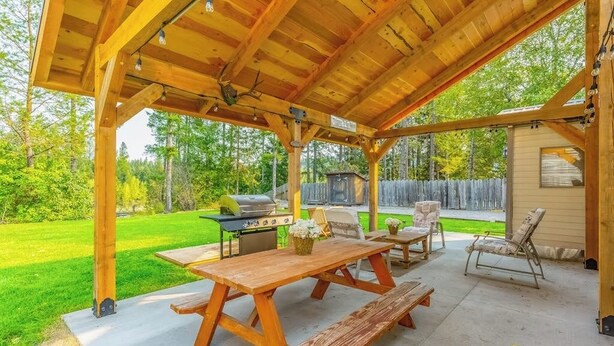 A covered outdoor patio with picnic tables, a grill, and lounge chairs.