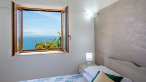 Quarto com cama, mesa de cabeceira, luminária e janela com persiana aberta.