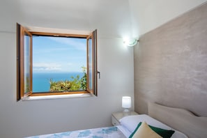 Ein Schlafzimmer mit einem Bett, einem Nachttisch, einer Lampe und einem Fenster mit geöffnetem Klappladen.