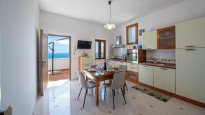 Uma cozinha moderna com uma mesa de jantar posta para quatro pessoas, uma janela grande e vista para o mar.