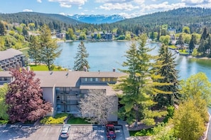 A lakeside hotel with a parking area, a building with a balcony, and a view of the lake and mountains. - Lakefront condo with balcony, stunning views, fast WiFi & W/D (Bigfork)