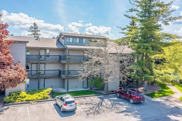 Un edificio residencial de varios pisos con estacionamiento, un árbol y cielo despejado.