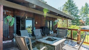Terraza de madera con mobiliario exterior, una parrilla y plantas colgantes.