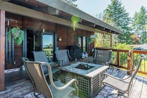 A wooden deck with outdoor seating, a grill, and hanging plants. - Lake & mountain view retreat with washer/dryer, & furnished deck (Bigfork)