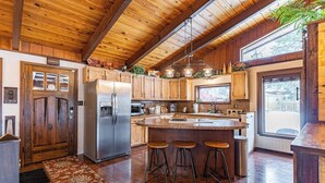 Una cocina con armarios de madera, un refrigerador de acero inoxidable, una isla grande con taburetes y un ventanal que proporciona luz natural.