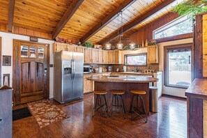 A kitchen with wooden cabinets, a stainless steel refrigerator, a large island with stools, and a window providing natural light. - Lake & mountain view retreat with washer/dryer, & furnished deck (Bigfork)