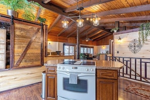 A rustic kitchen with wooden beams, a central island, and pendant lighting. - Lake & mountain view retreat with washer/dryer, & furnished deck (Bigfork)