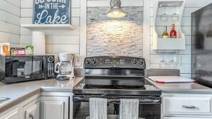 Une cuisine équipée d’une cuisinière, d’un four à micro-ondes et d’une machine à café. On y voit une pancarte sur laquelle est écrit : « ALLEZ VOUS DONNER UN PLONGEON DANS LE LAC ».