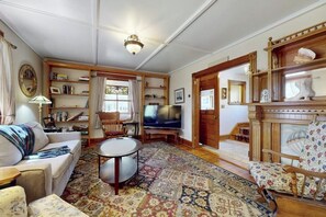 A living room with a sofa, armchair, TV, bookshelf, and a patterned rug. - Home with washer/dryer, gas grill, & outdoor dining - walk 5 minutes to beach (Rockport)