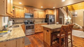 Una cocina con gabinetes de madera, encimeras de granito, electrodomésticos de acero inoxidable y un taburete de bar.