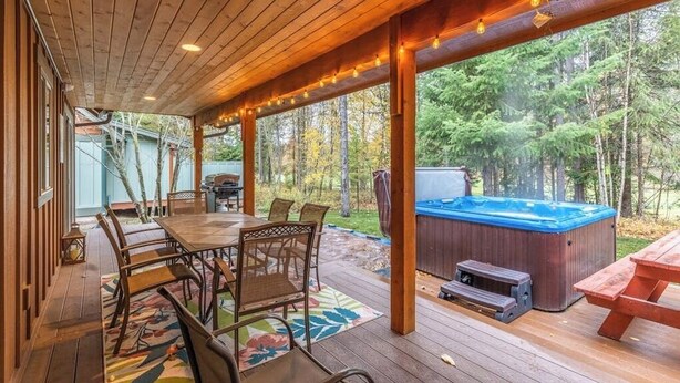 Una terraza de madera con un jacuzzi, una mesa con sillas y vistas al bosque.