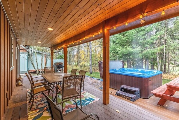 Eine Holzterrasse mit Whirlpool, Tisch und Stühlen sowie Blick auf den Wald.