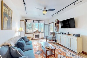A living room with a sofa, a television, a fireplace, and a patterned rug. - Brand-new downtown condo with rooftop patio, grill, mtn views, fireplace, & W/D (Columbia Falls)