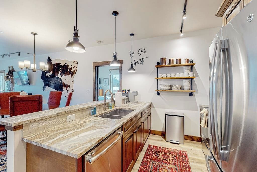 Een moderne keuken met een marmeren aanrecht, roestvrijstalen apparatuur, hanglampen en een rode vloerkleed.