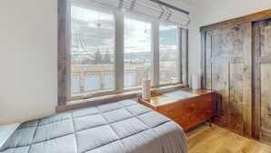 Ein Schlafzimmer mit großem Fenster, einem Bett, einer Holzkommode und Blick nach draußen.