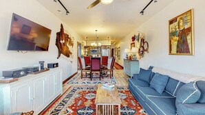 Ein Wohnzimmer mit einer Couch, einem Couchtisch, einem Fernseher, einem Deckenventilator und einem Essbereich mit Stühlen und einem Tisch.