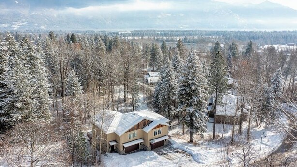 A house surrounded by snow-covered trees and mountains in the background. - Amiable townhome with fireplace, hot tub, patio, gas grill, deck, & balcony (Columbia Falls)