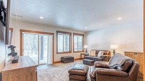 A spacious living room with a large window, a fireplace, a leather sofa, and a wooden coffee table. - Amiable townhome with fireplace, hot tub, patio, gas grill, deck, & balcony (Columbia Falls)
