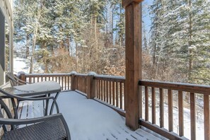 Eine Holzterrasse mit einem Metalltisch und -stühlen, umgeben von schneebedeckten Bäumen.