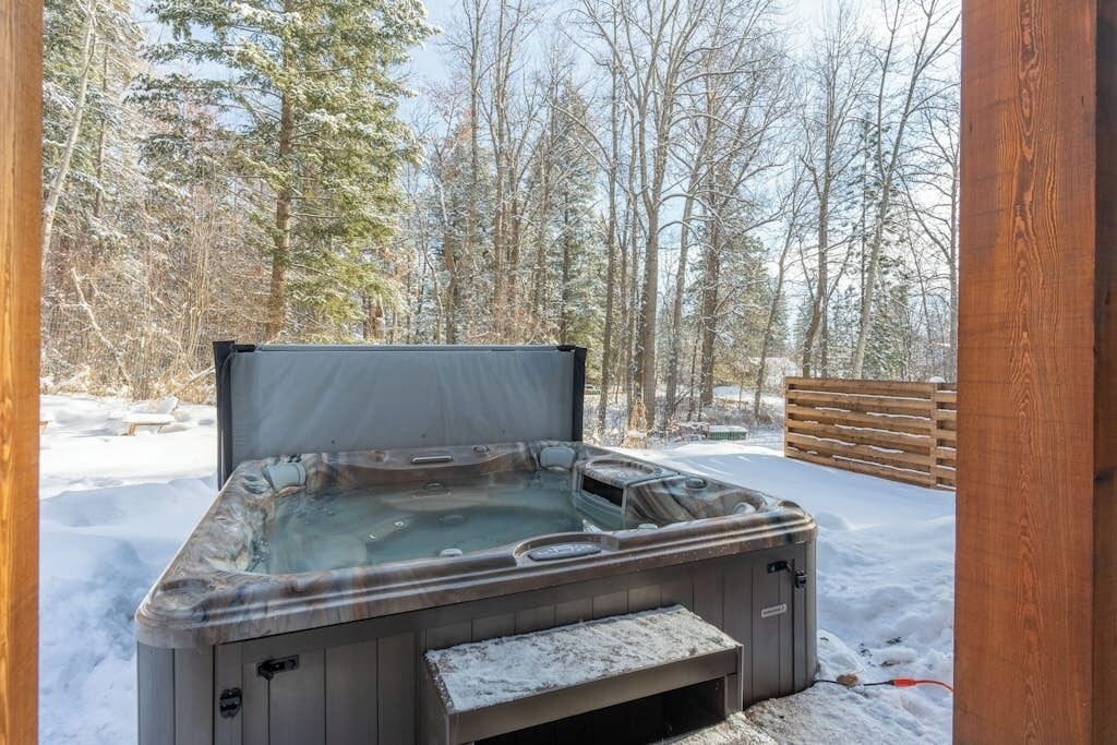 A hot tub in a snowy outdoor setting with a wooden deck and trees in the background.