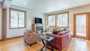 A spacious living room with a fireplace, large windows, and a red sofa. - Amiable townhome with fireplace, hot tub, patio, gas grill, deck, & balcony (Columbia Falls)