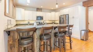 A modern kitchen with white cabinets, a central island with bar stools, stainless steel appliances, and pendant lighting. - Amiable townhome with fireplace, hot tub, patio, gas grill, deck, & balcony (Columbia Falls)