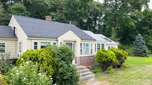 Een tweelaags huis met een veranda, een fundering van baksteen en een verzorgd gazon.