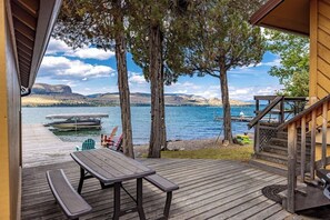 Eine Holzterrasse mit Picknicktisch, ein Boot liegt im Hintergrund und es bietet sich ein Blick auf einen See mit Bergen.