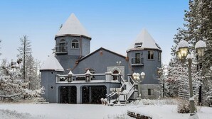 Un grande edificio grigio con due torri e un balcone, circondato da alberi innevati.