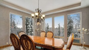 Una sala da pranzo con tavolo e sedie in legno, ampie finestre con vista innevata e un lampadario.