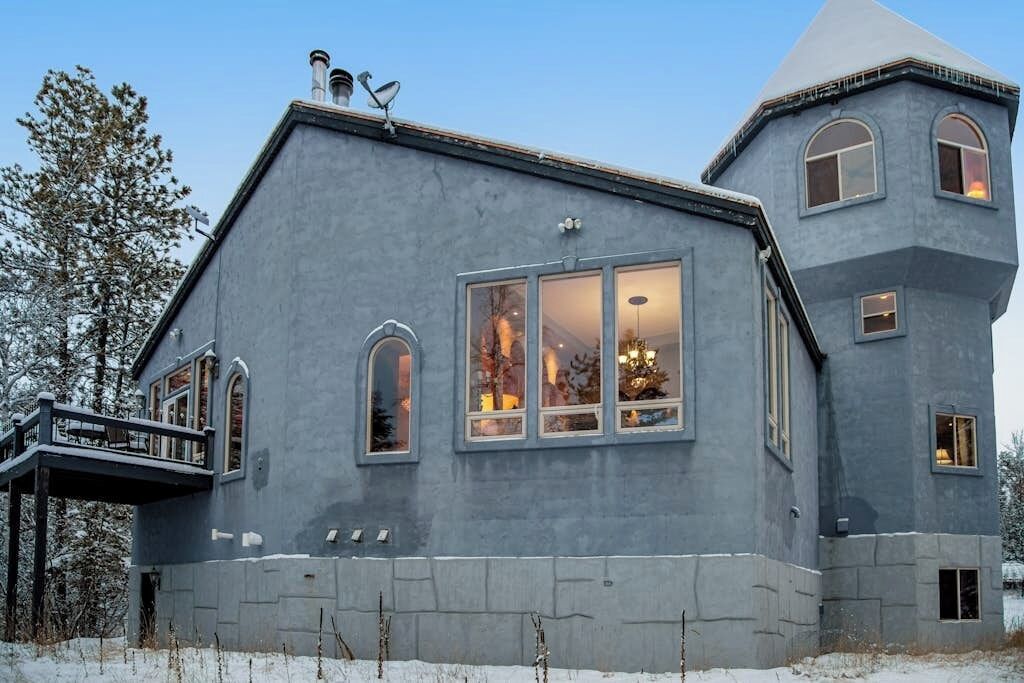 A large, modern house with a prominent tower section, large windows, and a balcony.