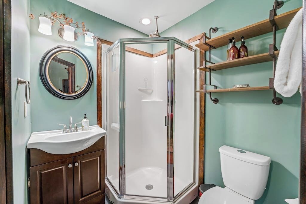 A bathroom with a glass-enclosed shower, a sink with a mirror, and a toilet.