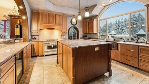 Un'ampia cucina con mobili in legno, una grande isola e vista su alberi innevati.