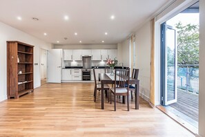Eine geräumige Küche mit weißen Schränken, einem Esstisch mit Stühlen und einer großen Schiebetür zum Balkon.