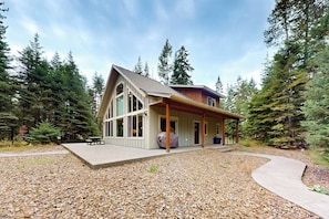 Ein modernes Haus mit einer großen Veranda, einer überdachten Sitzgruppe im Freien und einem Schotterweg.