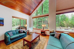 Ein geräumiges Wohnzimmer mit Holzboden, großen Fenstern, einem blauen Sofa, einem Holztisch und einem Teppich.