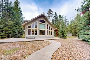 Ein Chalet mit großem Fensterfront, überdachter Veranda und gepflasterter Auffahrt.