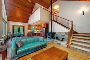 Ein geräumiger Wohnbereich mit hoher Decke, einer Holztreppe und einer Küche im Hintergrund.