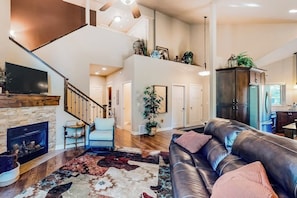 A spacious living area with a fireplace, leather sofa, and a staircase leading to an upper level.