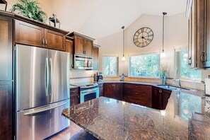 A modern kitchen with stainless steel appliances, dark wood cabinets, a large island, and a clock on the wall.