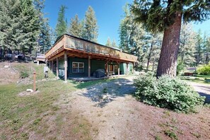 Eine Holzhütte mit einer Holzdielen-Terrasse, umgeben von Bäumen und einer Schotterauffahrt.