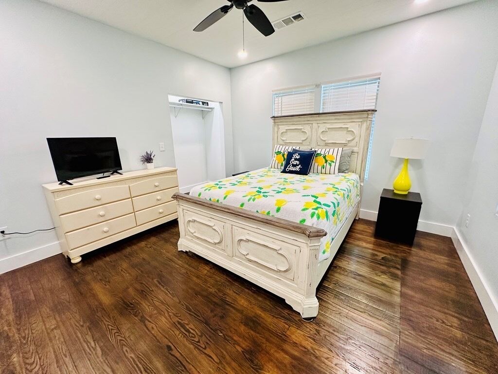Une chambre à coucher comprenant un lit, une commode, un téléviseur, un ventilateur de plafond et une lampe de chevet.