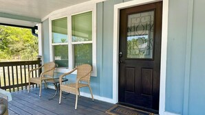 A porch with two wicker chairs, a dark door, and a welcome mat. - Renovated Gulf Coast Home - Walk to Marina, Dining, & Downtown Carrabelle (Carrabelle)